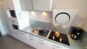 A modern kitchen with white cabinets, a built-in oven, a stainless steel sink, and a black induction cooktop. - Apartement Intense (LE CAP D AGDE)