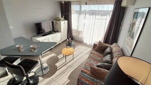 A modern living room with a sofa, a TV, a dining table, and a small coffee table. - Apartement Intense (LE CAP D AGDE)