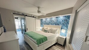 Una camera da letto con un letto, comodini, una ventola a soffitto e una finestra con persiane.