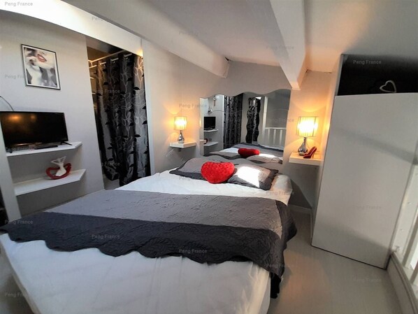 A modern hotel room with a large bed, bedside lamps, a TV, and a wardrobe.