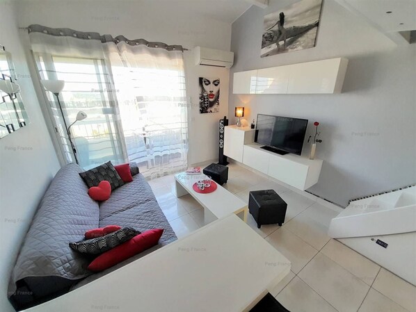 A modern living room with a sofa, coffee table, TV, and a balcony with outdoor furniture.