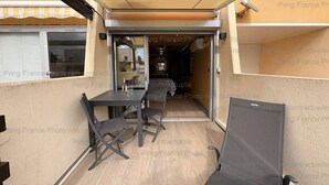 Pátio externo com mesa e cadeiras, porta de correr de vidro que dá para um espaço interno e toldo retrátil.