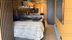 Um quarto compacto com cama, uma cozinha compacta e uma televisão.