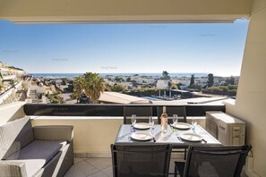 Ein Balkon mit Tisch für zwei Personen, mit Blick auf eine Stadtlandschaft mit Palmen und Gebäuden.