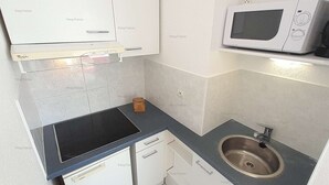 Una cucina compatta con mobili bianchi, un piano di lavoro nero, un forno a microonde e un lavello.