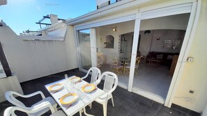 A patio with a table set for four, white plastic chairs, and a glass door leading to an interior space. - Villa COCO GIRL (LE CAP D AGDE)