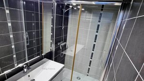 A modern bathroom with a large mirror, a white sink, and a glass-enclosed shower area. - Apartment "PEPPERONI" (LE CAP D AGDE)