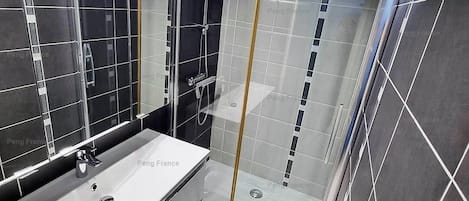 Un baño moderno con un espejo grande, un lavamanos blanco y una zona de ducha con paredes de vidrio.