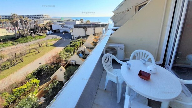 A balcony with white plastic chairs and a small table, overlooking a parking area and a building labeled "Peng France". - Apartment "PEPPERONI" (LE CAP D AGDE)