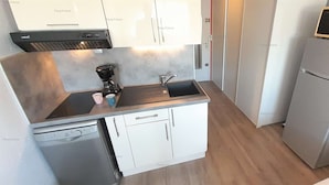 Ett kompakt kök med diskmaskin, kaffebryggare, mikrovågsugn och kylskåp.