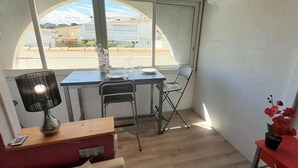 Ett litet rum med ett bord och två stolar, en lampa, ett litet träbord med en fjärrkontroll och en krukväxt.