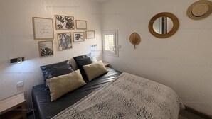 A bedroom with a bed, pillows, framed artwork, a mirror, and a window.