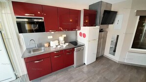 A modern kitchen with red cabinets, a built-in oven, a refrigerator, and a microwave. - Villa "Séduction" (LE CAP D AGDE)
