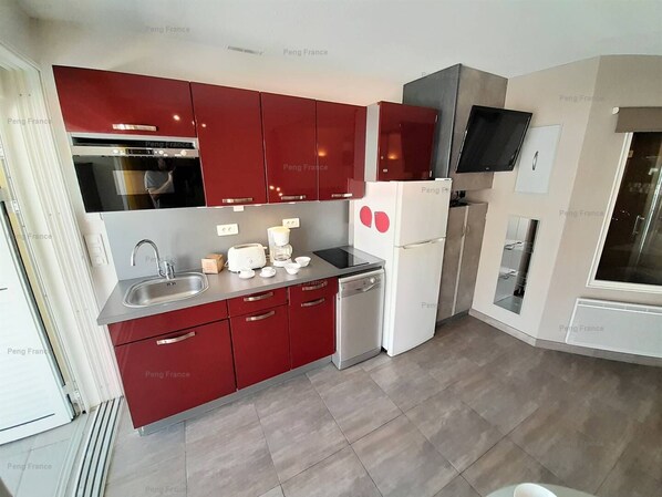 A modern kitchen with red cabinets, a built-in oven, a refrigerator, and a microwave. - Villa "Séduction" (LE CAP D AGDE)