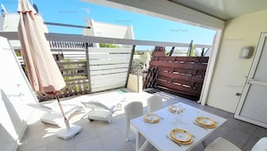A patio area with a table set for dining, white chairs, a sun umbrella, and a wooden fence in the background. - Villa "Séduction" (LE CAP D AGDE)