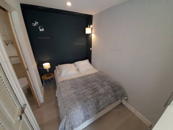 A bedroom with a bed, a nightstand, and a wall-mounted lamp.