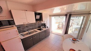 A modern kitchen with a microwave, stove, sink, and cabinets. There is a dining area with a table and chairs. - Studio 'DEVIL or EDEN" (LE CAP D AGDE)