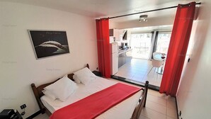 A bedroom with a bed, a red blanket, a nightstand, a power outlet, and a window with curtains. - Studio 'DEVIL or EDEN" (LE CAP D AGDE)