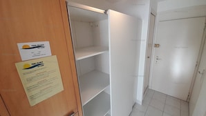 Ein Hotelzimmer mit Holztür, weißer Wand und Fliesenboden. Auf der Tür ist ein Schild angebracht und an der Wand ein Hinweis.