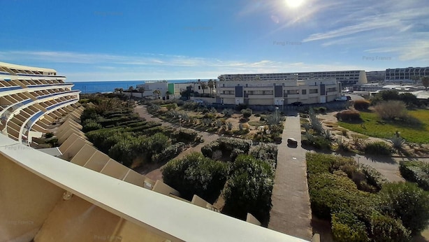 Ein moderner Gebäudekomplex mit einem zentralen Innenhof, umgeben von Grünflächen und freiem Blick auf das Meer.