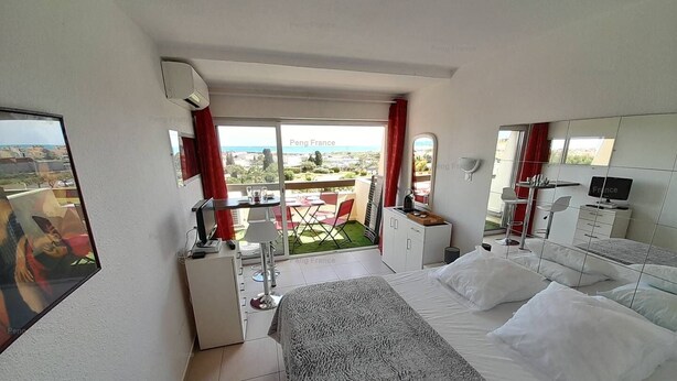 A compact hotel room with a bed, a desk, a chair, and a small balcony with a view. - Studio Piña Colada (LE CAP D AGDE)
