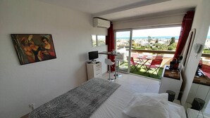 A bedroom with a bed, a desk, a chair, a TV, and a painting on the wall. - Studio Piña Colada (LE CAP D AGDE)