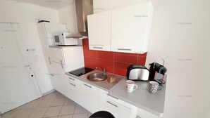 Una cucina compatta con mobili bianchi, uno schienale rosso, un lavandino in acciaio inossidabile, un tostapane e una macchina per il caffè.