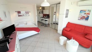 Una camera d'albergo con un letto, una scrivania con un portatile, un divano rosso e un angolo cottura sullo sfondo.