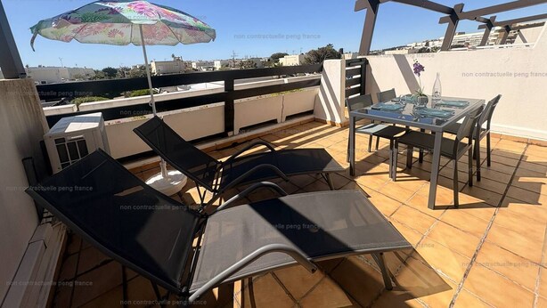 Une terrasse sur le toit, avec une table et des chaises, un parasol coloré et une vue sur la ville.