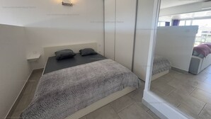Une chambre moderne comprenant un lit, des tables de chevet, un miroir et une porte coulissante donnant sur un balcon.