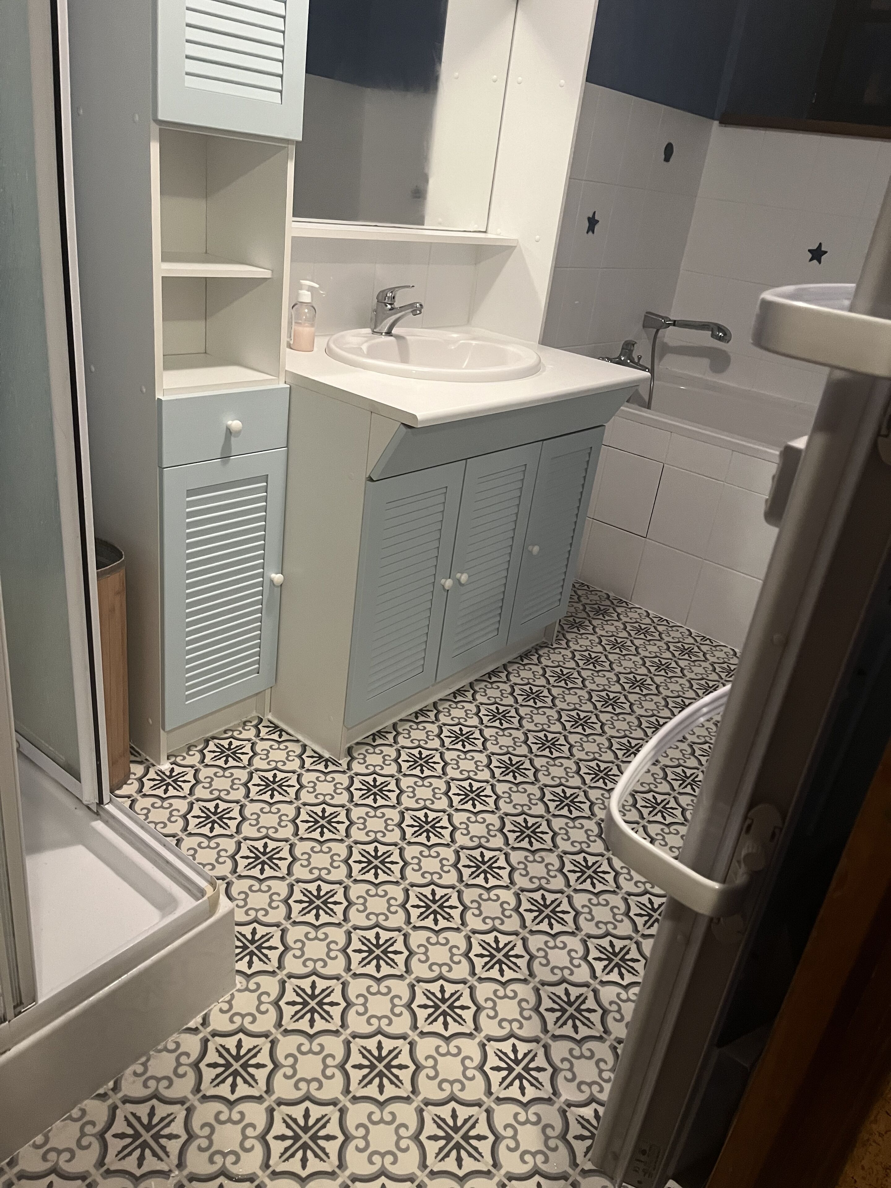 Un baño con lavamanos blanco, un espejo y zona de ducha.
