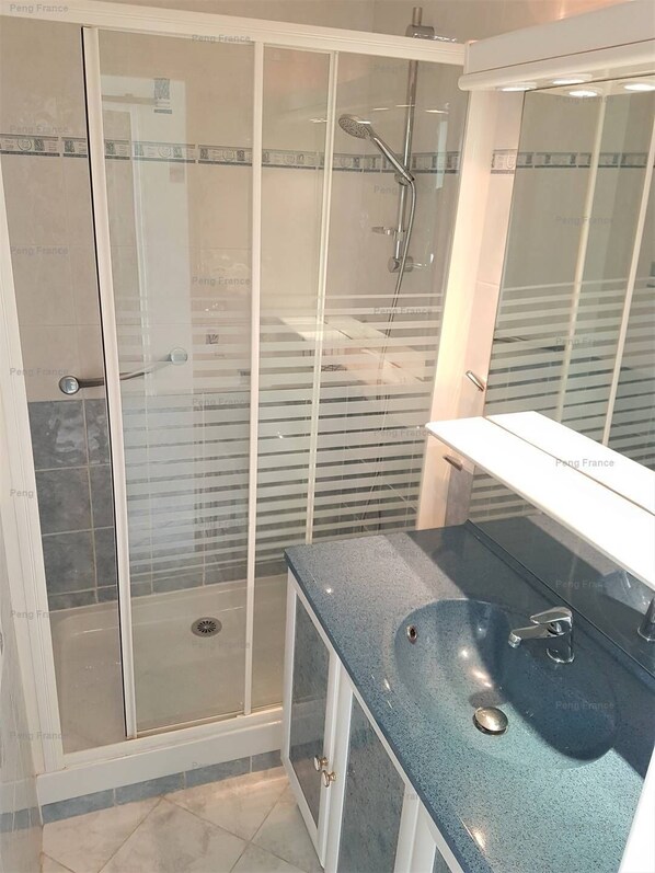 A bathroom with a glass-enclosed shower, a sink with a blue countertop, and a mirror above the sink.