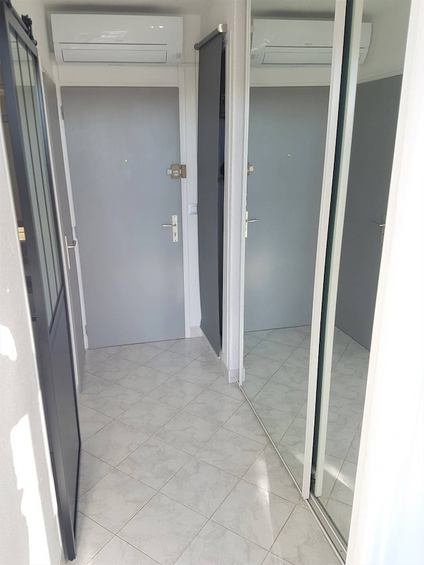 A hallway with two doors, a tiled floor, and an air conditioning unit on the wall.