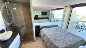 A modern hotel room with a large bed, a bathroom with a glass shower enclosure, a small desk, and a balcony with a view. - Studio Ô Plaisir (LE CAP D AGDE)