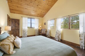 Cozy retreat with a large bed, wooden ceiling, and a comfortable chair by the window.