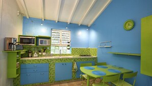 Une cuisine compacte avec des meubles de couleur verte, un dosseret de carrelage bleu et un petit coin repas comprenant une table et des chaises vertes.