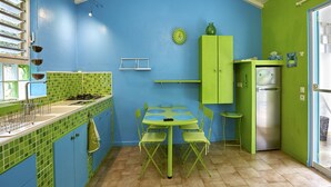 Une cuisine aux couleurs bleu et vert, une table à manger avec des chaises, un réfrigérateur et un luminaire suspendu.