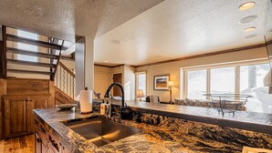 A kitchen with a granite countertop, wooden cabinets, a stainless steel sink, and a wooden staircase. - Beautiful Modern Home in Great Location, Hot Tub +Patio, Luxury Amenities! (Park City)