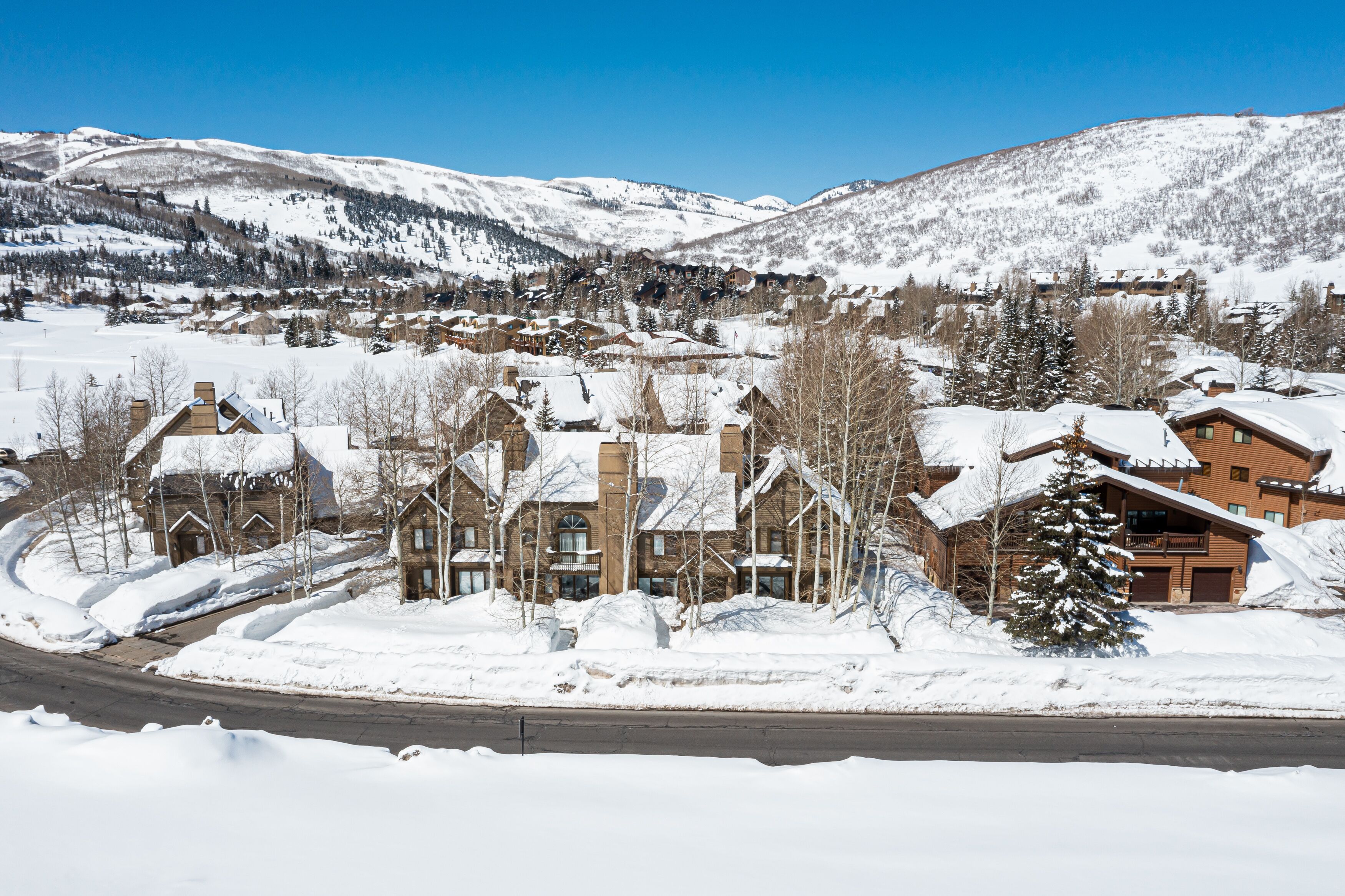 A snow-covered mountain town with traditional wooden buildings, a main road, and a clear blue sky.
