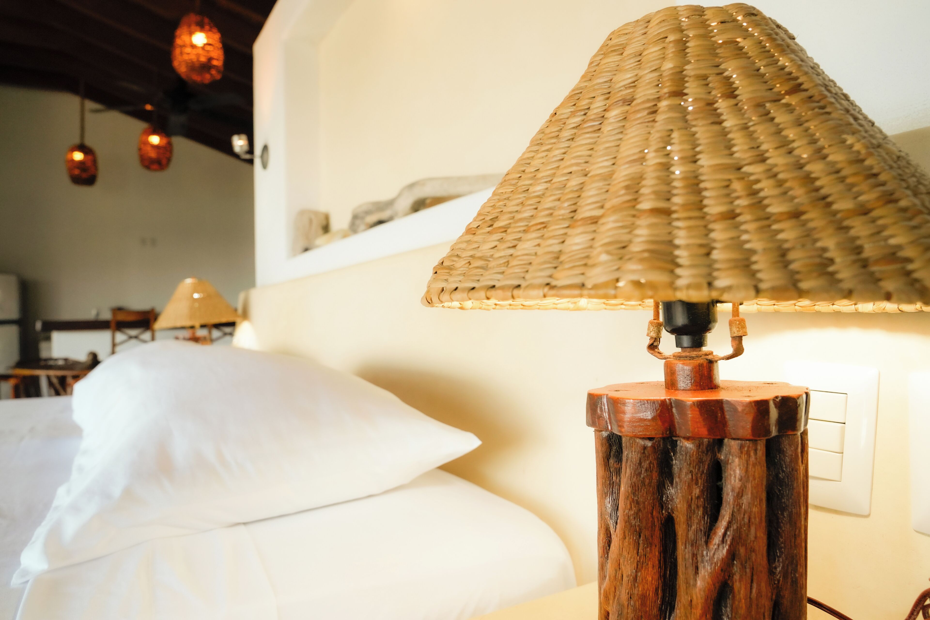 A bed with white linens, a wooden lamp base, and a woven lampshade.