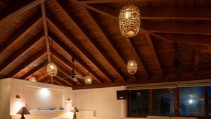 Une chambre spacieuse avec un plafond haut, des poutres apparentes, un grand lit, des lampes de chevet, une télévision et une vue sur l’extérieur par une fenêtre.