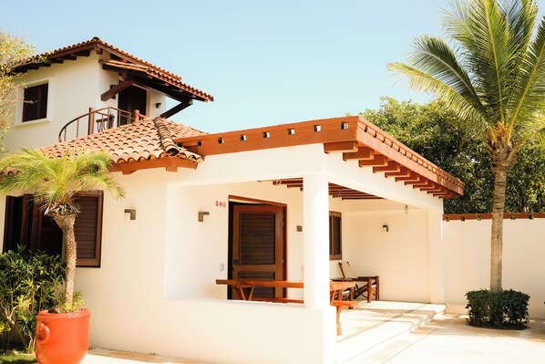A two-story house with a covered patio, a wooden door, and a small table.