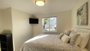 Een slaapkamer met een bed, een televisie, een raam en een schilderij aan de muur.
