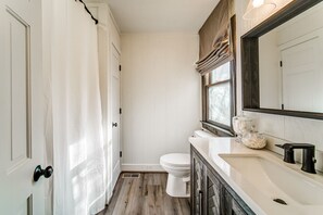 Bathroom features a toilet, sink, and shower, with a large mirror and window.