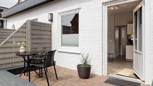 Une maison moderne dotée d’un patio comprenant une table et des chaises, une plante en pot et un escalier menant à un étage supérieur.
