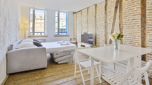 Ein Zimmer mit einem Bett, einem Schreibtisch und einem Stuhl. Es gibt Fenster und einen Blick auf Gebäude.