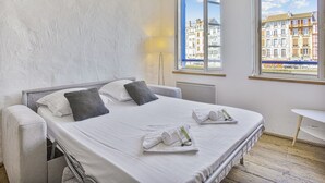 Ein Hotelzimmer mit einem Bett, zwei Nachttischen, einer Lampe und Blick auf Gebäude durch das Fenster.
