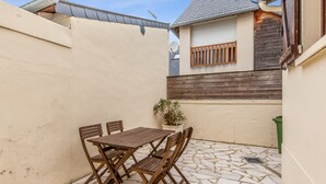 A patio with a wooden table and chairs, a potted plant, and a small window with wooden bars. - Maison Flatelle - Welkeys (Trouville-sur-Mer)