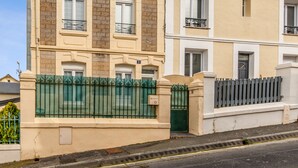 A two-story building with a beige facade, a green metal fence, and a grey metal gate. - Maison Flatelle - Welkeys (Trouville-sur-Mer)