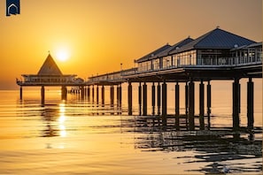 Eine Pier, die sich über ruhiges Wasser erstreckt, mit einem Sonnenuntergang im Hintergrund.